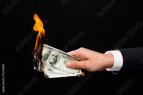 close up of male hand holding burning dollar money
