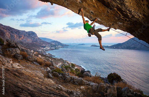Rock climber on overhanging cliff before sunset