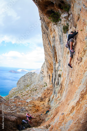 Young man lead climbing on cliff near sea
