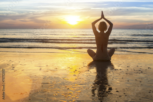 Woman doing meditation near the ocean. Yoga silhouette.