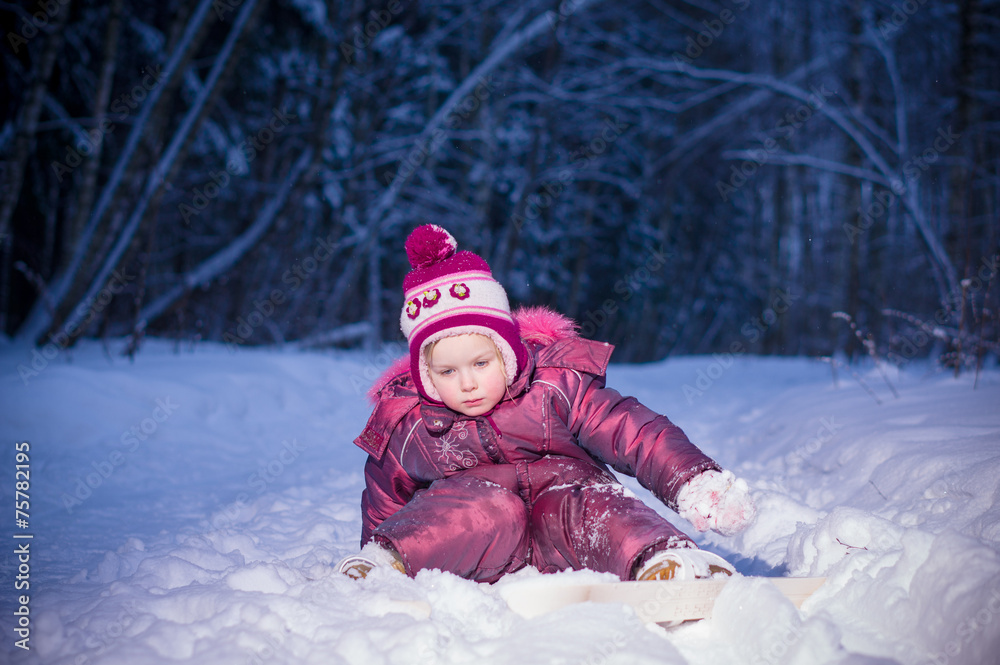 Adorable girl ride on ski in evening park. Sit on snow Adorable girl ride on ski in evening park. Sit on snow