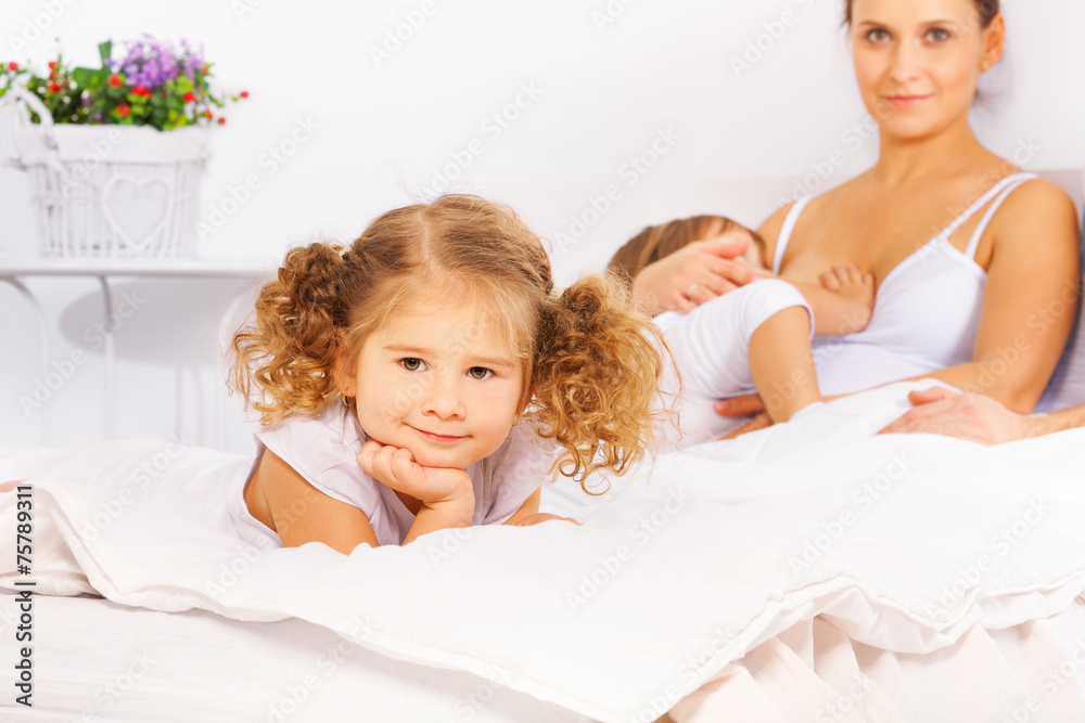 Adorable girl on white bed with mother feeding son Adorable girl on white bed with mother feeding son