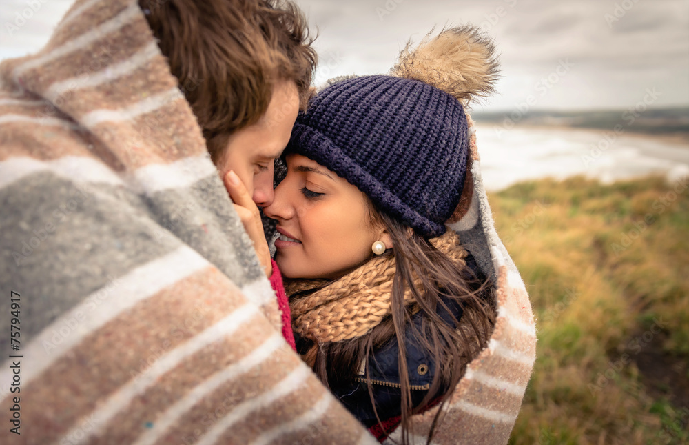 Young couple embracing outdoors under blanket in a cold day Young couple embracing outdoors under blanket in a cold day