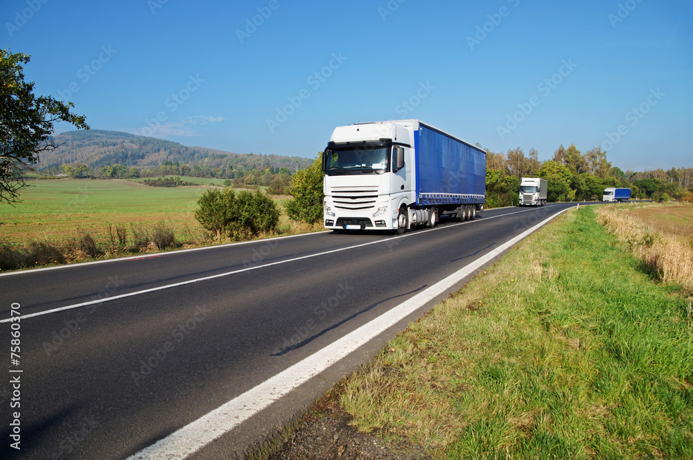 Three white trucks on the road in the countryside