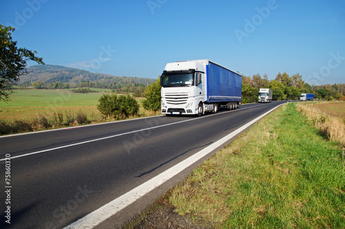 Three white trucks on the road in the countryside