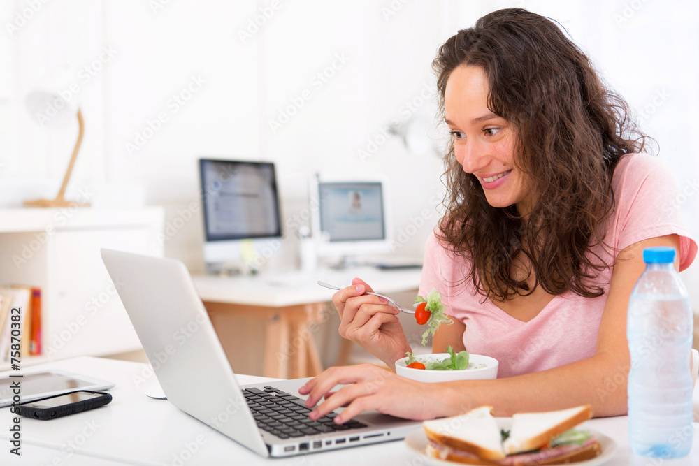 Young attractive student eating salad while working
