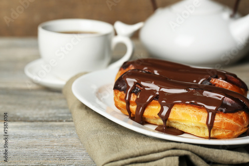 Tasty eclairs and cup of tea on wooden table