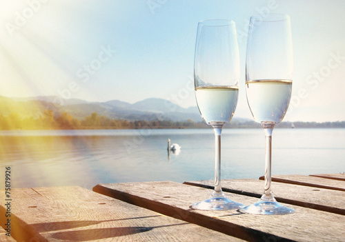 Two champagne glasses against a lake