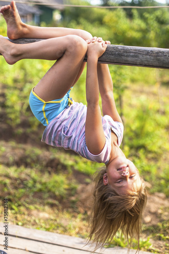 Картината върху платно Little girl in park hanging upside down on rural countryside.