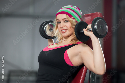 Female trains in gym with dumbbells