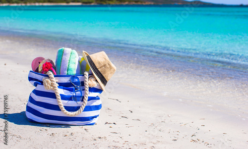 Blue bag, straw hat, flip flops and towel on white beach © travnikovstudio
