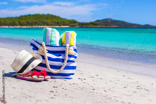 Blue bag, straw hat, flip flops and towel on white beach