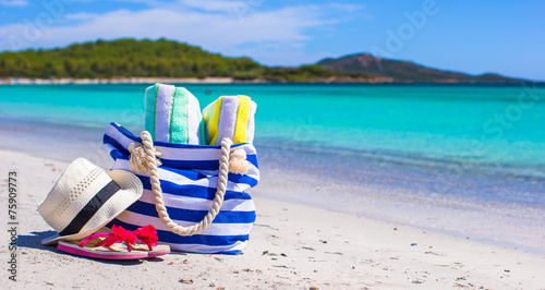 Blue bag, straw hat, flip flops and towel on white beach