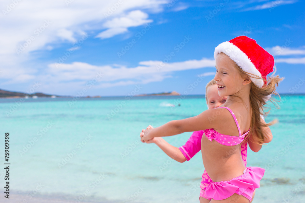 Little adorable girls in Santa hats during beach vacation Little adorable girls in Santa hats during beach vacation