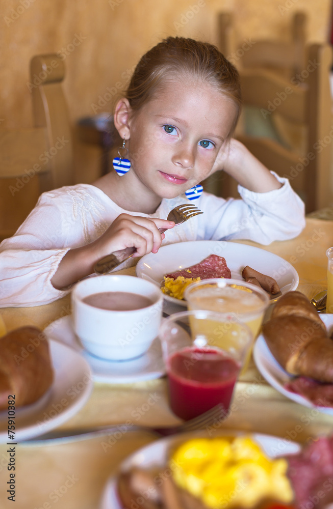 Adorable little girl having breakfast at indoor cafe