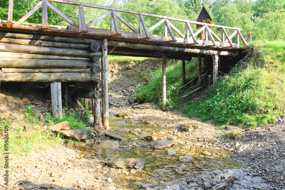 Old bridge over the forest stream in hot summer day