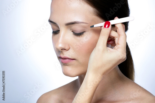 Closeup portrait of a cute young woman plucking eyebrows