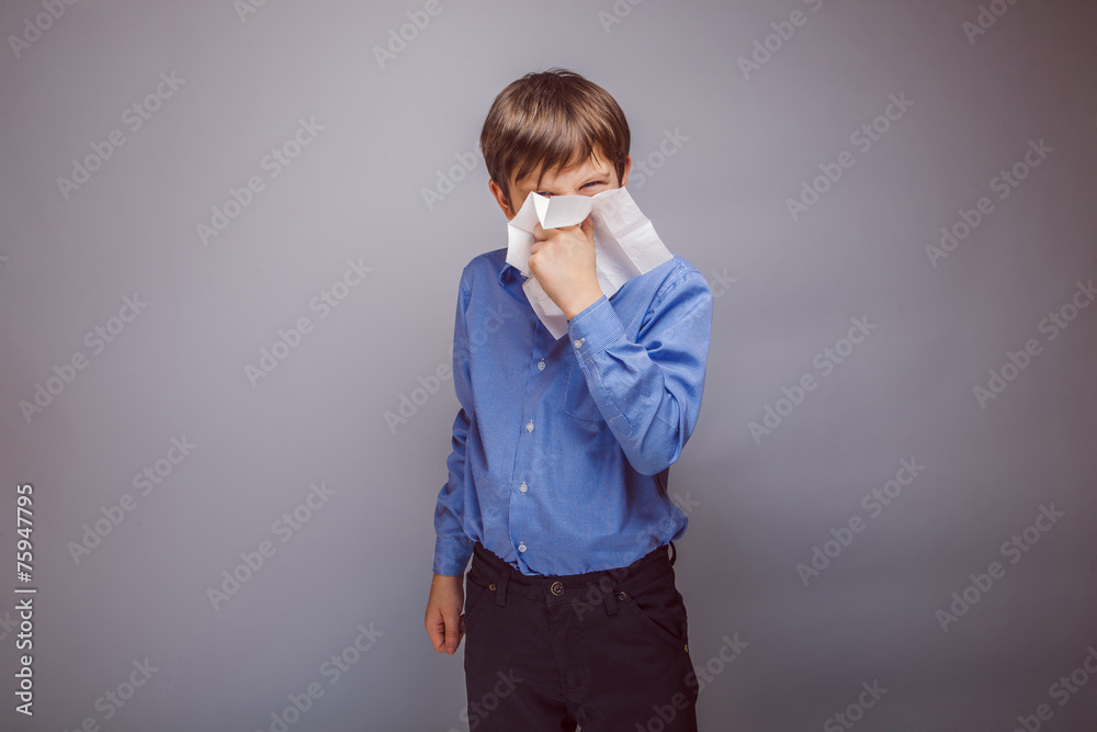 teenager boy sick sneezing into a handkerchief on gray backgro teenager boy sick sneezing into a handkerchief on gray backgro