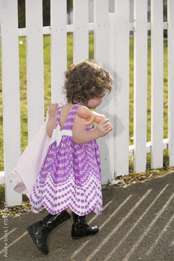 little girl in front of white fence with her doll little girl in front of white fence with her doll