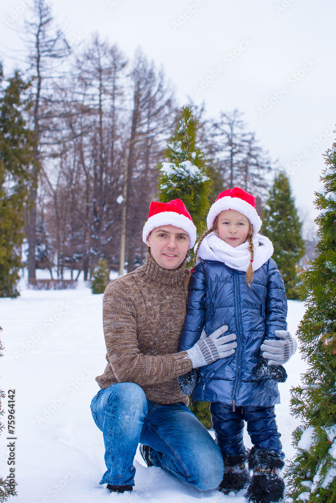 Happy father and kid in Santa hats with christmas tree outdoor