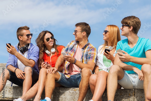group of smiling friends with smartphones outdoors