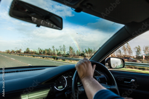 Male driver hands on steering wheel of a car and road © Voyagerix