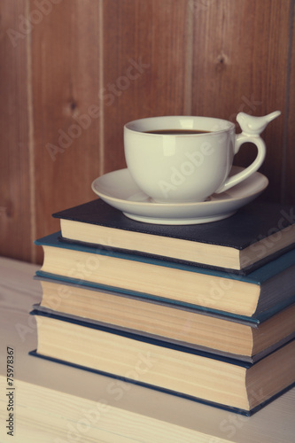 Pile of books with cup on tabletop and wooden background