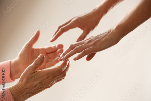 Old and young holding hands on light background, closeup