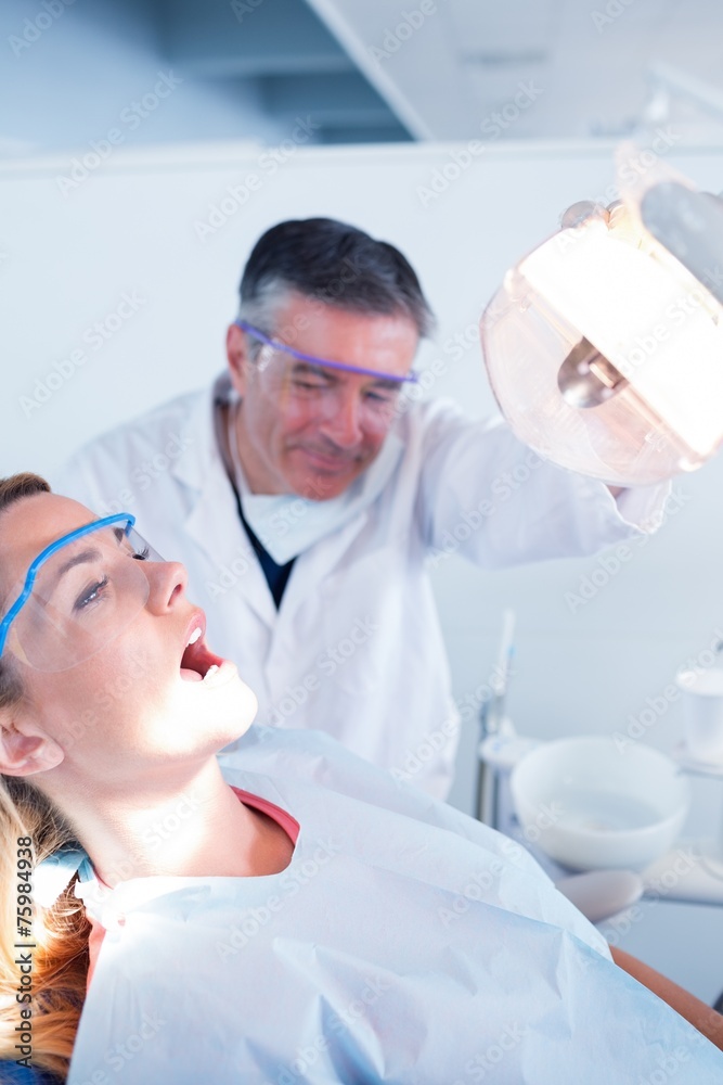 Fototapeta premium Dentist examining a patients teeth in chair under bright light