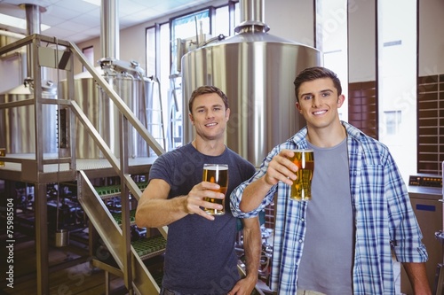 Young men holding a pint of beer smiling at camera