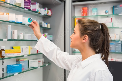 Junior pharmacist taking medicine from shelf