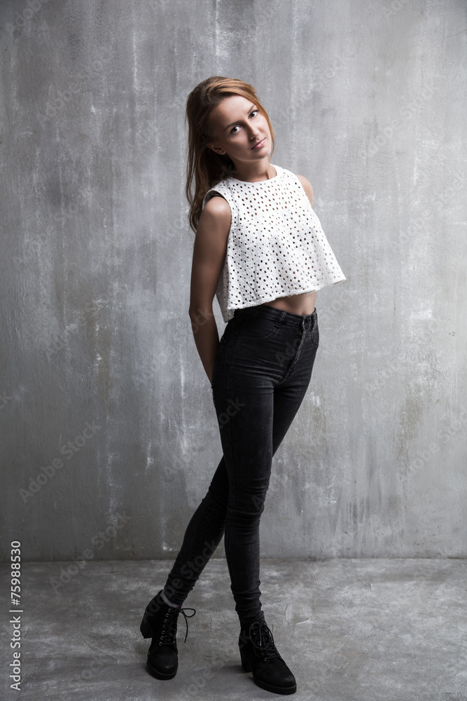 Fototapeta premium Fashionable young girl standing on a gray background textured wa