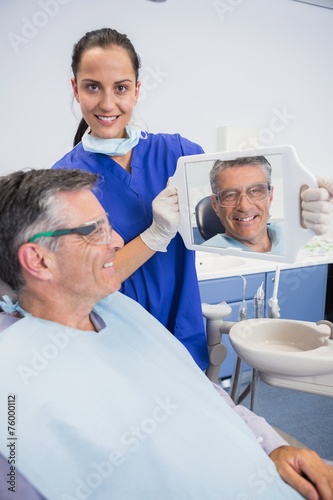 Smiling dentist showing teeth of her patient with a mirror