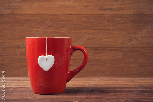 Red cup with white heart shape over wooden background