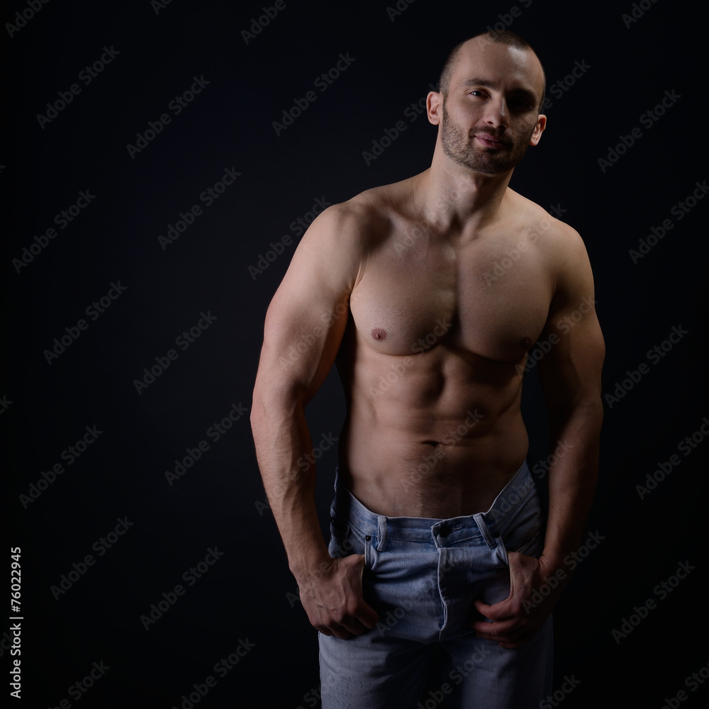 Fototapeta premium Strong athletic man with perfect body posing in studio on black