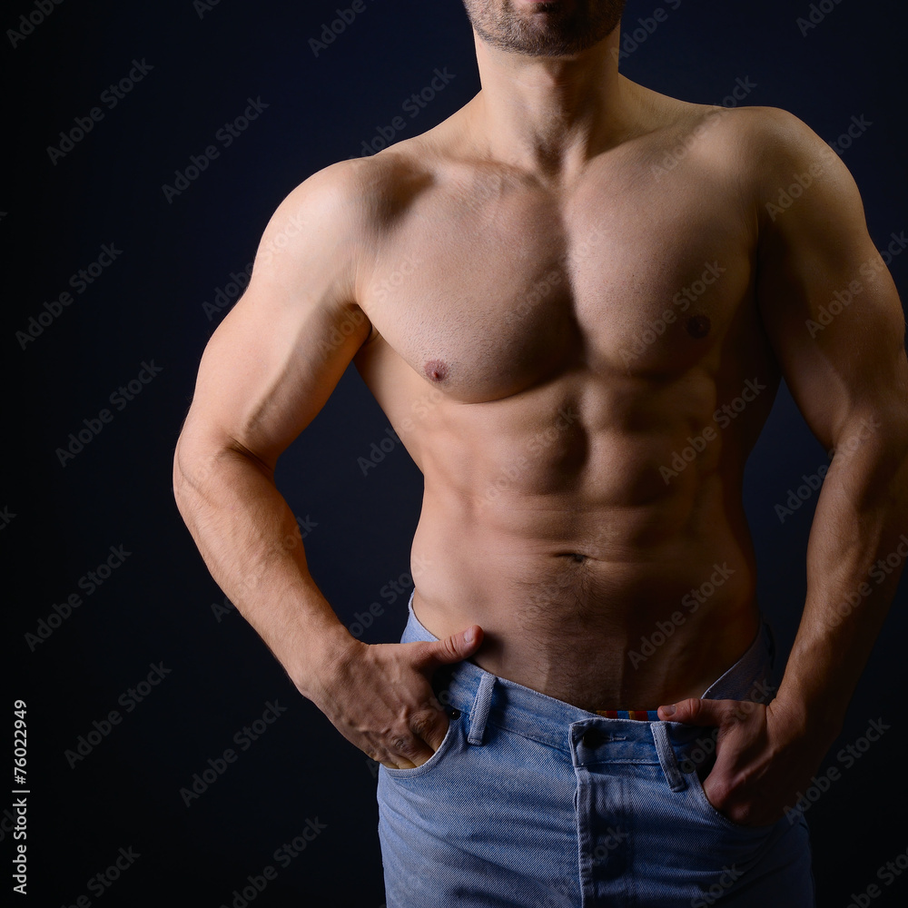 Strong athletic man with perfect body posing in studio on black