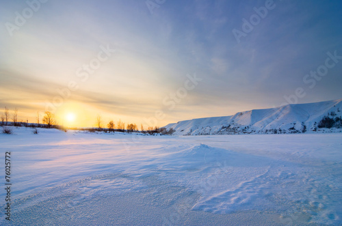 Winter landscape with frozen river and hills at sunset