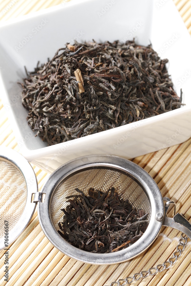 Fototapeta premium black tea leaves in white bowl with strainer on bamboo mat