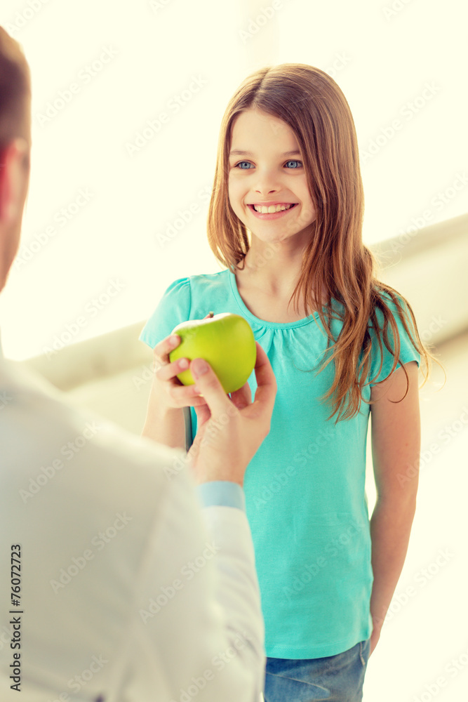 male doctor giving an apple to smiling little girl male doctor giving an apple to smiling little girl