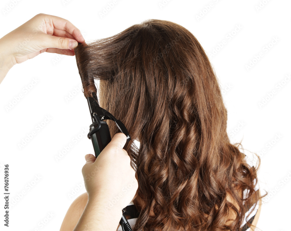 Naklejka premium Stylist using curling iron for hair curls, close-up, isolated