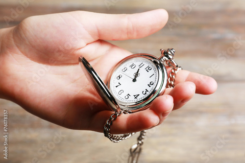 Silver pocket clock in hand on wooden background
