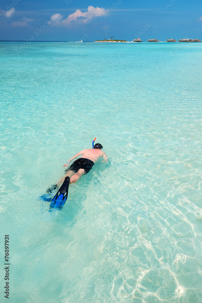 Young man snorkling in tropical lagoon with over water bungalows