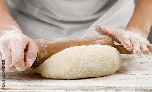 Hands preparing dough with rolling pin on wooden table