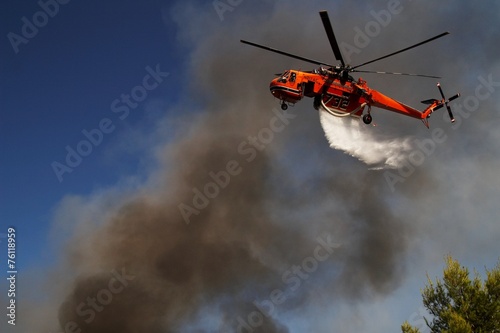 Firefigthers are fighting with bushfire. Helicopter drops water from the sea