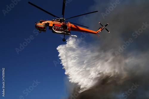 Firefigthers are fighting with bushfire. Helicopter drops water from the sea