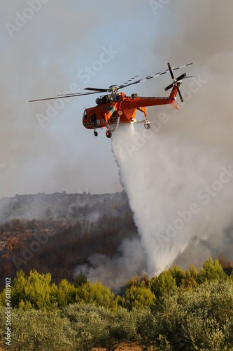 Firefigthers are fighting with bushfire. Helicopter drops water from the sea