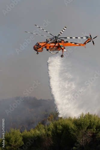 Firefigthers are fighting with bushfire. Helicopter drops water from the sea