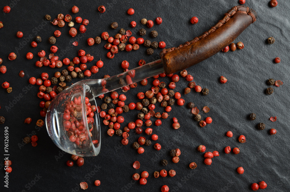 Cooking spoon with pink peppercorns on dark, stone background Cooking spoon with pink peppercorns on dark, stone background