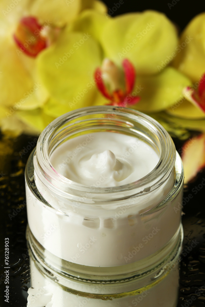 Face cream with orchid flowers on dark background