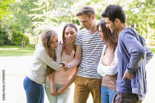 Happy students looking at smartphone outside on campus
